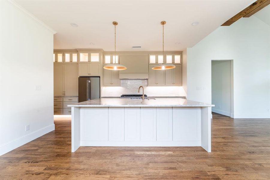 Kitchen featuring a central island with a light-toned countertop, wood-finish flooring, and two modern pendant lights Kitchen featuring a central island with a light-toned countertop, wood-finish flooring, and two modern pendant lights