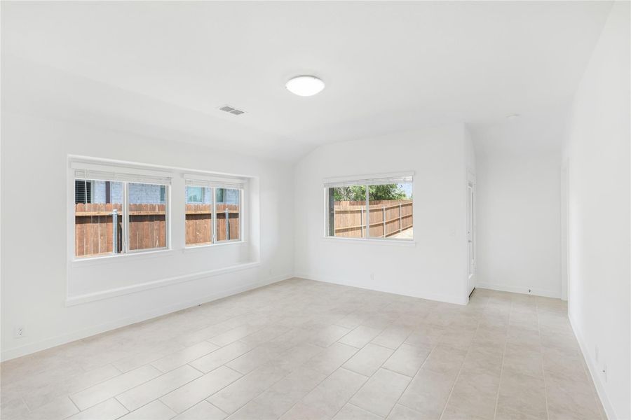 Empty room with white walls, tile floors, and three windows overlooking a wood fence
