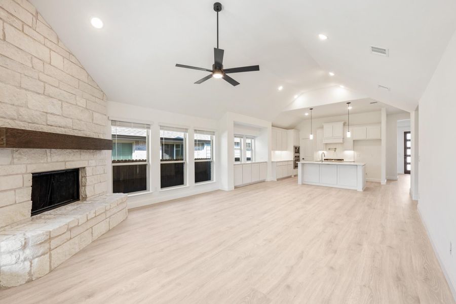 Open living area with stone fireplace, vaulted ceiling, and open-concept kitchen with white cabinets and light wood floors