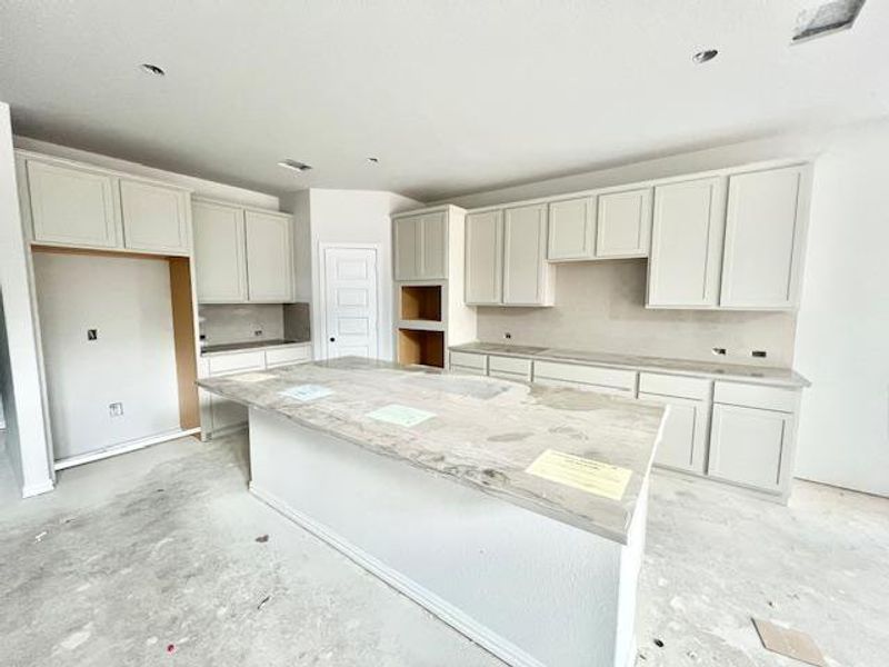 Kitchen with a center island, decorative backsplash, concrete floors, and light stone counters Kitchen with a center island, decorative backsplash, concrete floors, and light stone counters