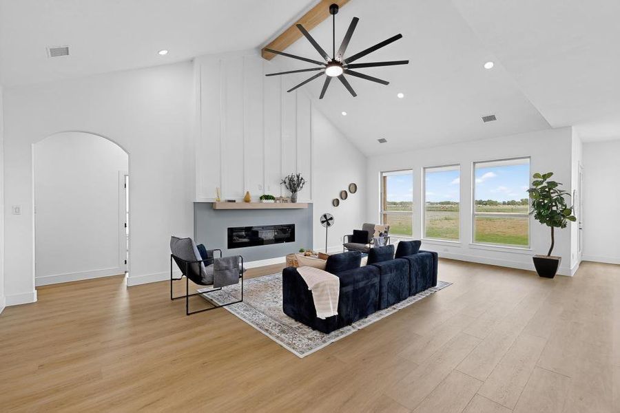 Living area with beam ceiling, a ceiling fan, arched walkways, light wood finished floors, and a large fireplace