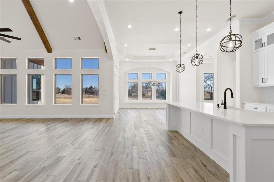 Open Kitchen with a large island, decorative light fixtures, sink, white cabinets, custom flooring