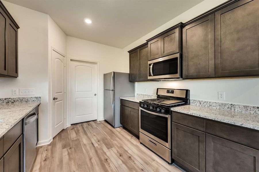 Kitchen with light stone counters, appliances with stainless steel finishes, dark cabinets, and light wood-style floors