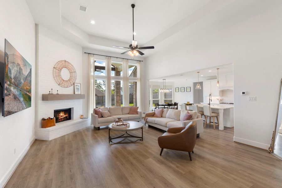 This spacious living area features an open floor plan with high ceilings, a cozy fireplace, and abundant natural light from large windows. The modern kitchen and dining area flow seamlessly, creating an inviting space for family gatherings.