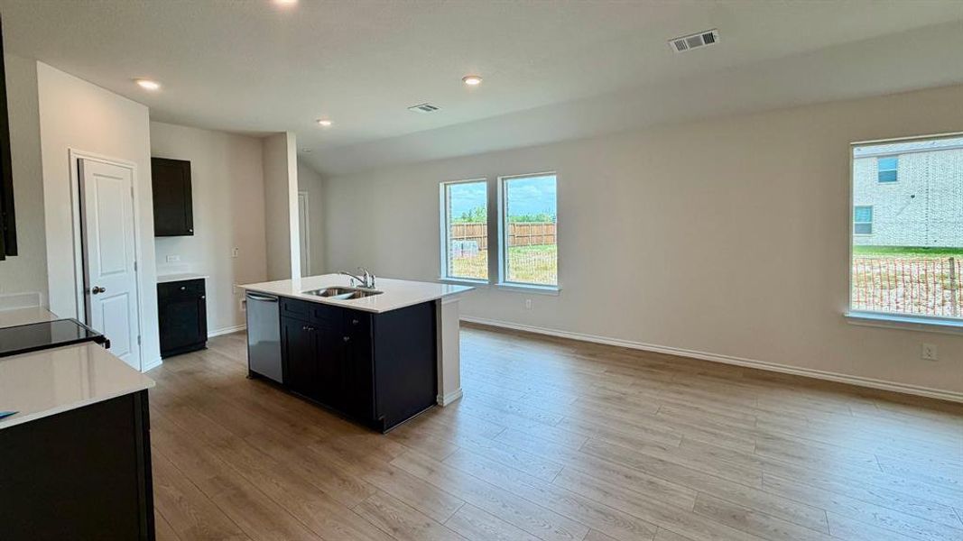 Open-concept kitchen and living area featuring wood-finish flooring, recessed lighting, white countertops, dark cabinetry, and multiple windows