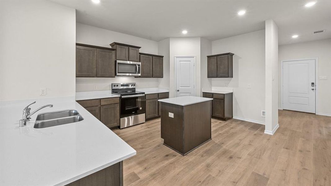 Kitchen featuring stainless steel appliances, recessed lighting, dark wood finish cabinets, a kitchen island, and light wood-style flooring