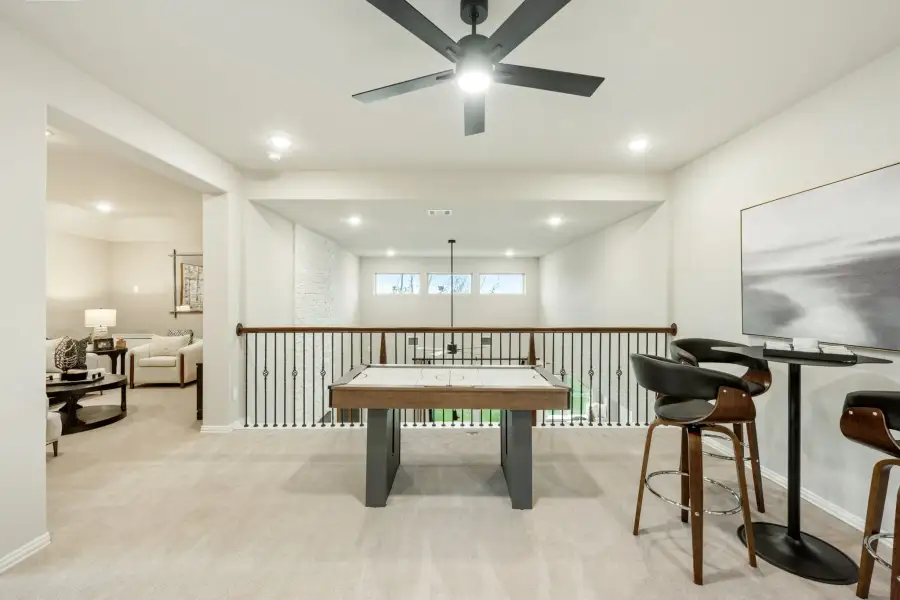 Loft game room with air hockey table, bar seating, ceiling fan, and open railing overlooking lower level