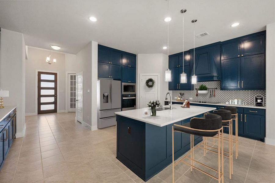 Kitchen boasts pretty blue cabinetry, a breakfast bar, decorative light fixtures, appliances with stainless steel finishes, and tasteful backsplash.  (Photo has been virtually staged)