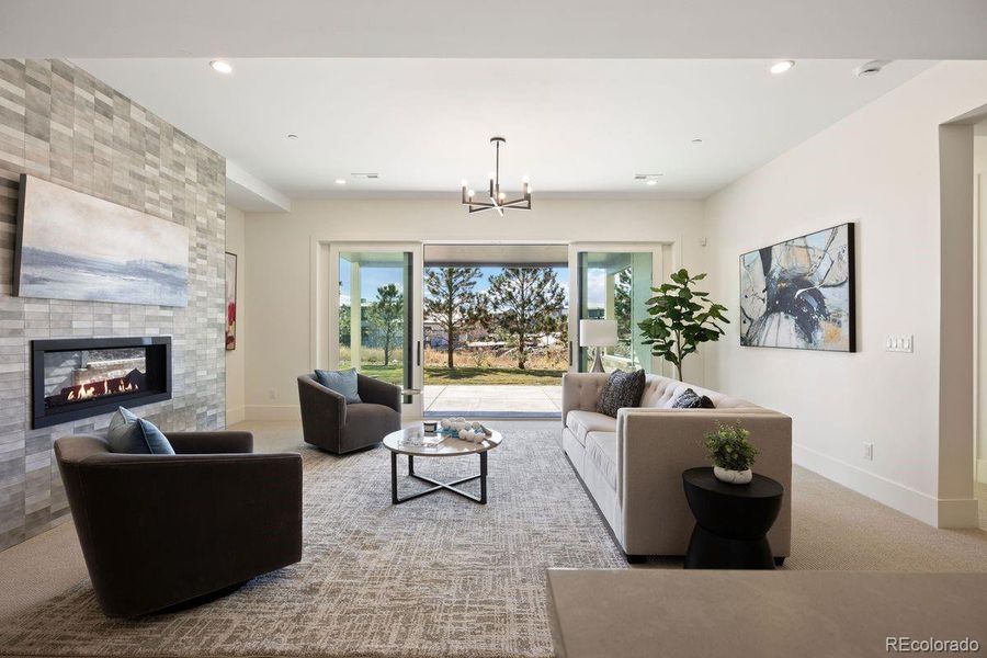 Another view of the sophisticated lower-level rec room featuring a sleek linear fireplace and expansive sliding glass doors that open to a private outdoor patio.