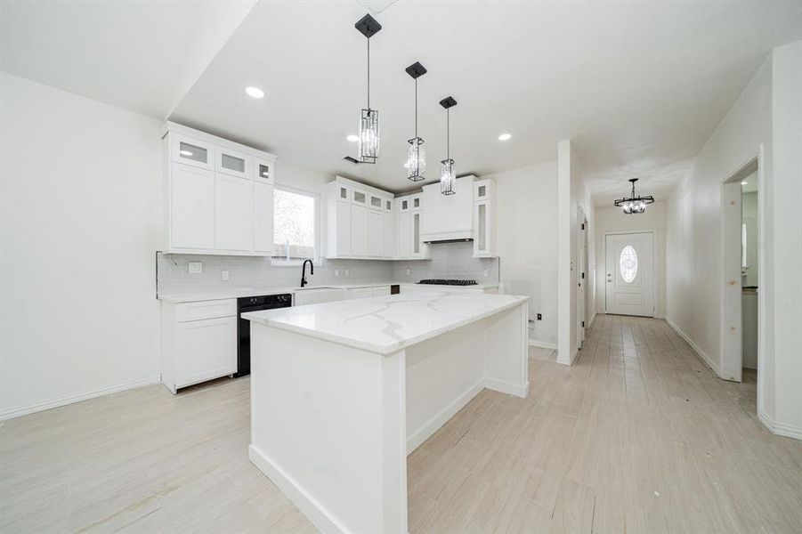 Kitchen with hanging light fixtures, a kitchen island, glass insert cabinets, white cabinets, and tasteful backsplash
