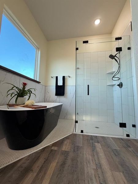 Full view of the master bathroom of soaking bathtub and custom shower doors with matte black faucets.  Custom white tile flooring and shower walls.