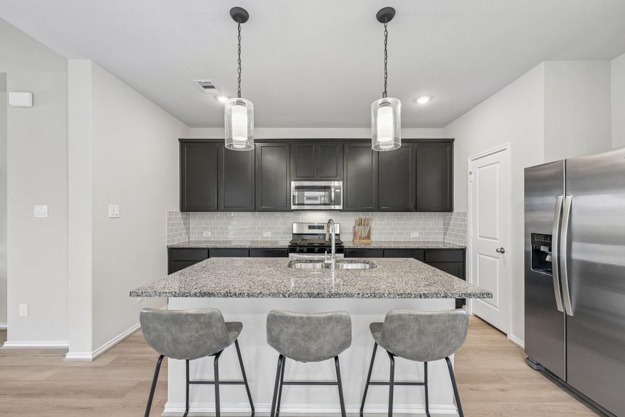 Modern kitchen featuring a spacious granite island with pendant lighting, sleek dark cabinets, and stainless steel appliances, including a side-by-side refrigerator.