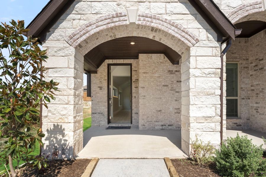 Stone home entrance with arched covered porch, tall glass front door, and concrete walkway
