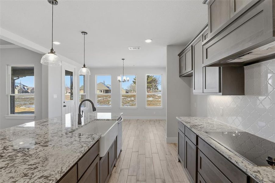 Kitchen featuring under cabinet range hood, light stone counters, wood finish floors, black electric stovetop, and pendant lighting