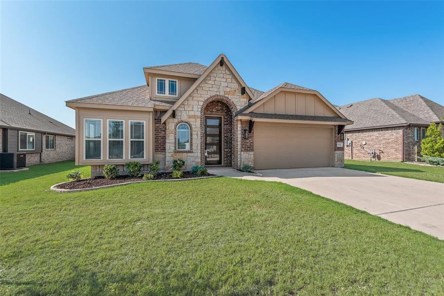View of front of property featuring stone siding, roof with shingles, a front lawn, and concrete driveway View of front of property featuring stone siding, roof with shingles, a front lawn, and concrete driveway