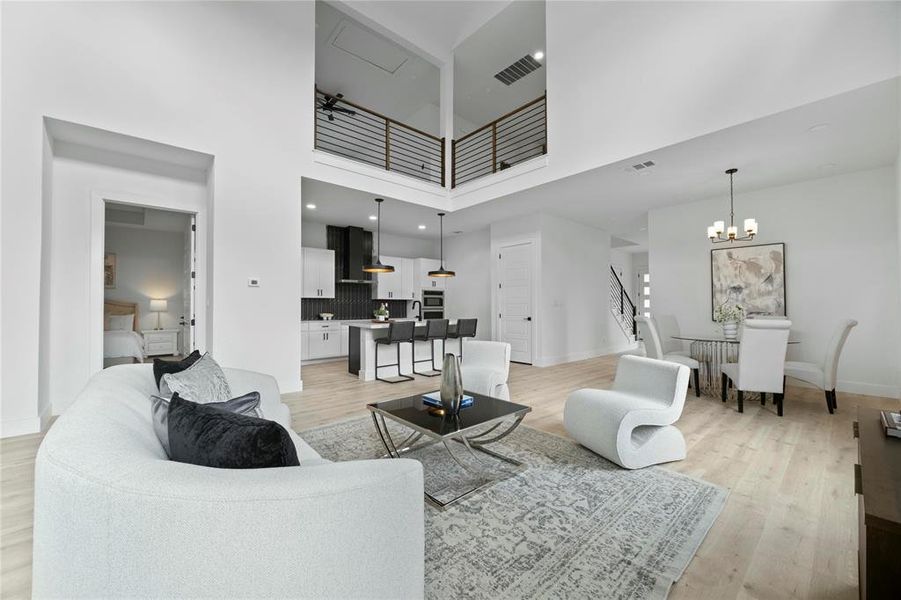 Living area featuring light wood-style flooring, a towering ceiling, and a chandelier Living area featuring light wood-style flooring, a towering ceiling, and a chandelier