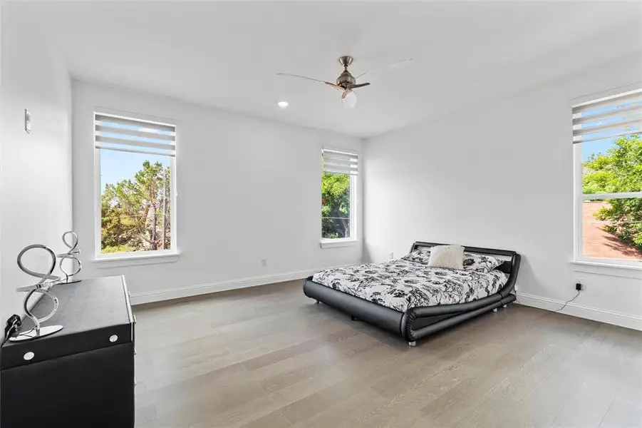 Bright interior room featuring wood-finish flooring, white walls, and multiple windows with horizontal window treatments