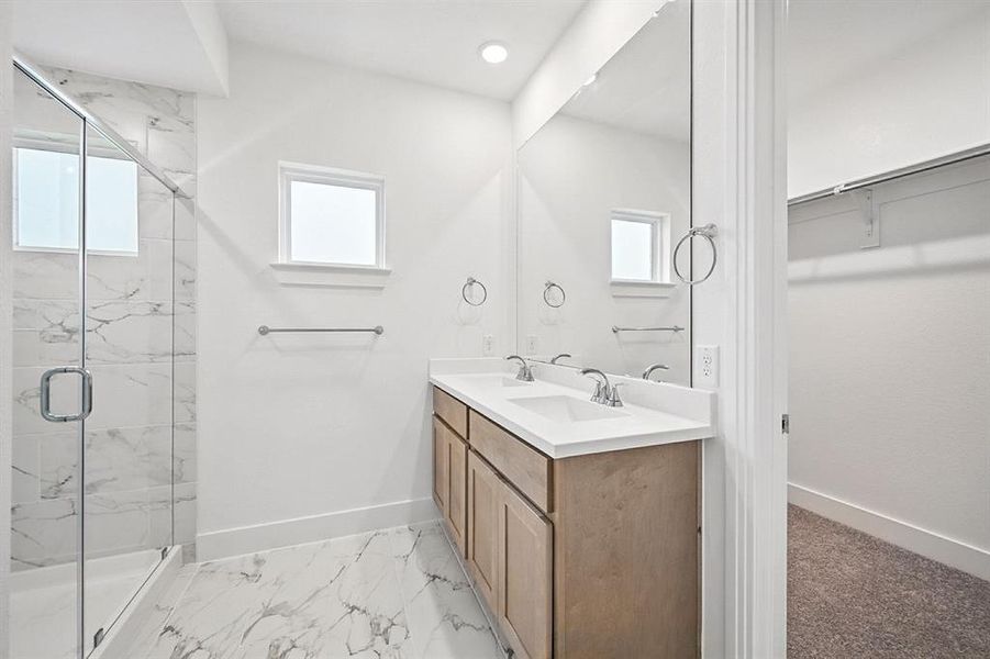 Full bathroom with healthy amount of natural light, a marble finish shower, double vanity, and light marble finish floors Full bathroom with healthy amount of natural light, a marble finish shower, double vanity, and light marble finish floors