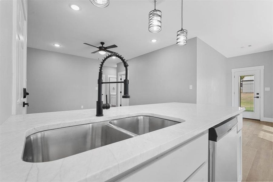 Kitchen with light stone countertops, stainless steel dishwasher, white cabinets, light hardwood / wood-style floors, and decorative light fixtures