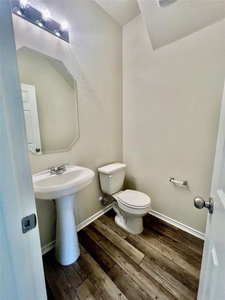 A compact guest bath featuring rich wood flooring and a classic pedestal sink.