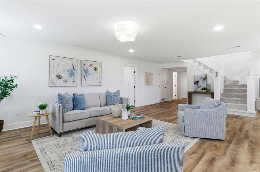 Living area featuring hardwood style flooring, recessed lighting, and a staircase with carpeted treads Living area featuring hardwood style flooring, recessed lighting, and a staircase with carpeted treads