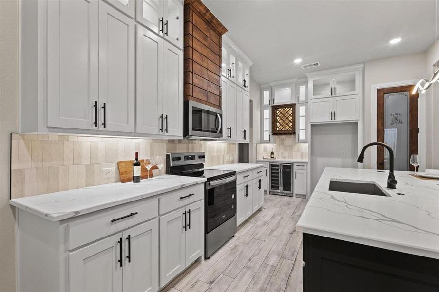 Kitchen with white cabinetry, appliances with stainless steel finishes, light stone countertops, decorative backsplash, and glass insert cabinets