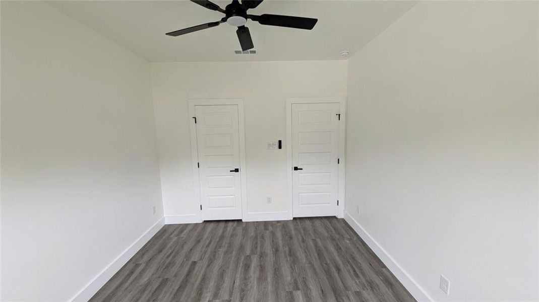 Unfurnished bedroom featuring baseboards, a ceiling fan, dark wood-type flooring, and visible vents