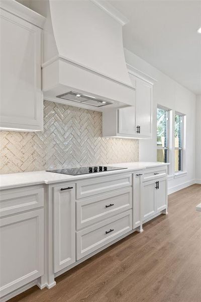 Contemporary kitchen showcasing white cabinetry, a built-in cooktop, white countertops, and a herringbone-patterned tile backsplash Contemporary kitchen showcasing white cabinetry, a built-in cooktop, white countertops, and a herringbone-patterned tile backsplash
