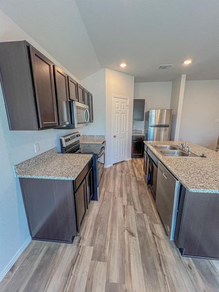 Kitchen featuring dark brown cabinetry, appliances with stainless steel finishes, light stone counters, light wood-type flooring, and recessed lighting