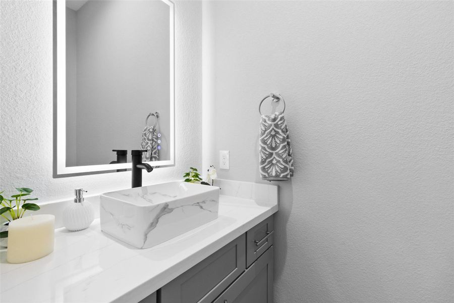 Your powder bath feels like a designer’s touch—every detail, from the glowing mirror to the deep blue vessel sink, makes even quick stops feel luxurious.