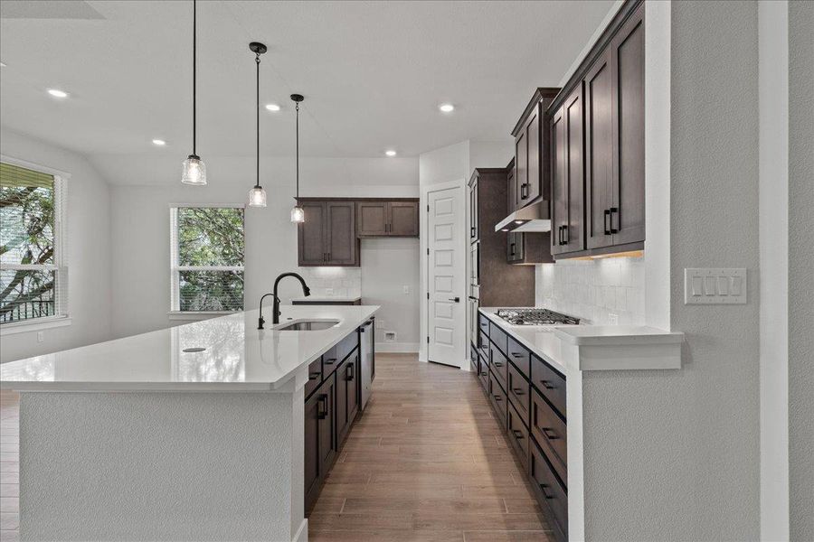 Kitchen with decorative light fixtures, light stone counters, backsplash, and recessed lighting Kitchen with decorative light fixtures, light stone counters, backsplash, and recessed lighting