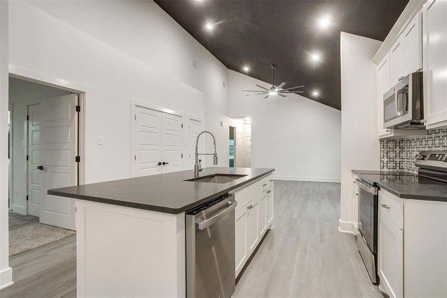 Kitchen with appliances with stainless steel finishes, dark countertops, light wood-style floors, decorative backsplash, and high vaulted ceiling