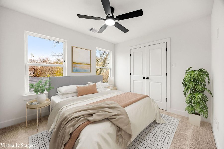 This light-filled bedroom offers a calming retreat with neutral finishes, plush carpeting, ceiling fan, and multiple windows that bring in abundant natural light, creating a comfortable and versatile space ideal for guests or everyday living.