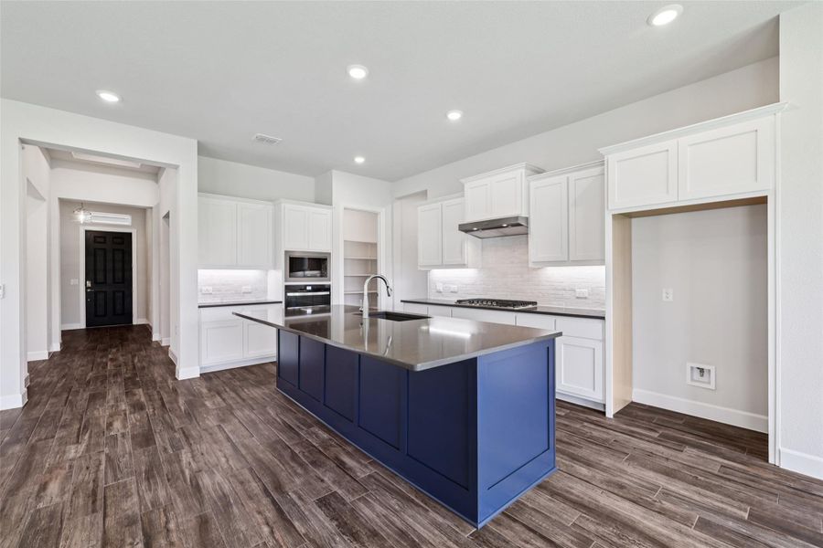 Kitchen with dark wood-type flooring, decorative backsplash, an island with sink, white cabinetry, and recessed lighting
