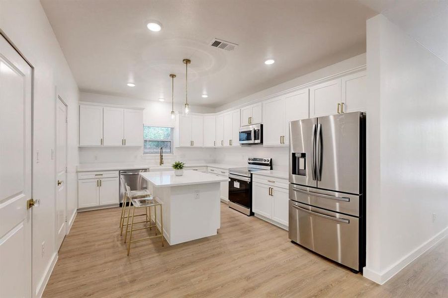 Kitchen featuring a center island, light hardwood / wood-style floors, stainless steel appliances, and hanging light fixtures