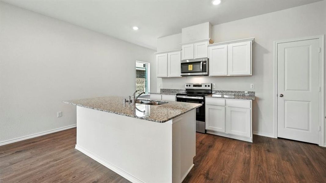Kitchen featuring a central island with a built-in sink, light speckled countertops, white cabinetry, stainless steel appliances, and wood-finish flooring