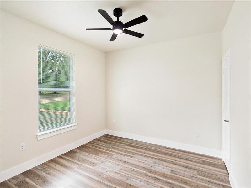 Room featuring wood-finish flooring, a contemporary black ceiling fan with integrated lighting, a window with blinds, and neutral wall paint Room featuring wood-finish flooring, a contemporary black ceiling fan with integrated lighting, a window with blinds, and neutral wall paint