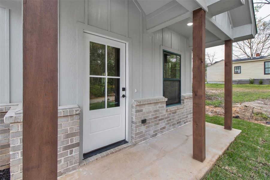 Doorway to property featuring board and batten siding, covered porch, and brick siding