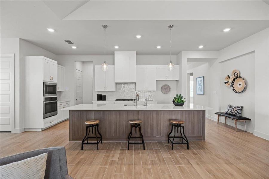 Kitchen featuring a breakfast bar area, a large island, wood tiled floors, hanging light fixtures, and dual tone cabinets