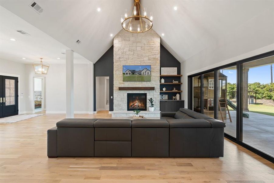 Living room with a fireplace, light hardwood / wood-style flooring, built in shelves, a chandelier, and high vaulted ceiling