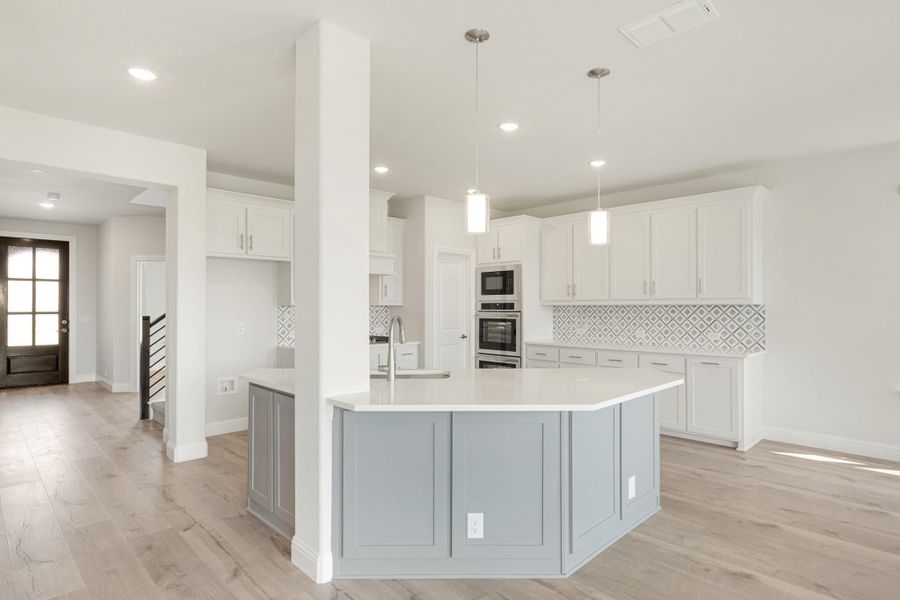 Open kitchen with large gray island, white cabinets, patterned tile backsplash, and stainless steel appliances