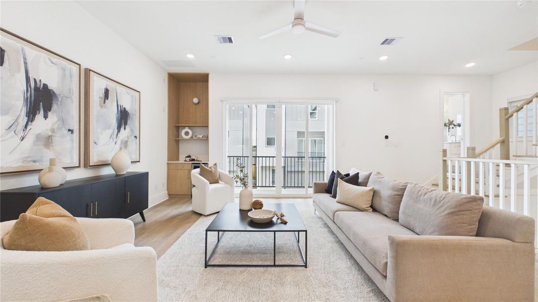 This bright, modern living room features a neutral color palette with a large sectional sofa, stylish armchairs, and abstract art. It has a spacious, open layout with sliding glass doors leading to a balcony, offering ample natural light.