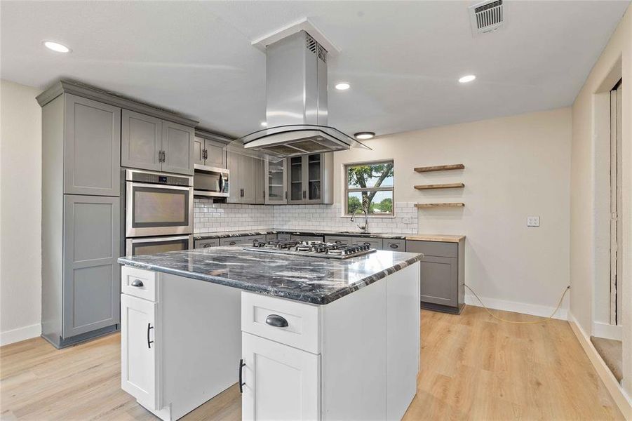 Kitchen with gray cabinets, open shelves, tasteful backsplash, dark stone counters, and a center island Kitchen with gray cabinets, open shelves, tasteful backsplash, dark stone counters, and a center island
