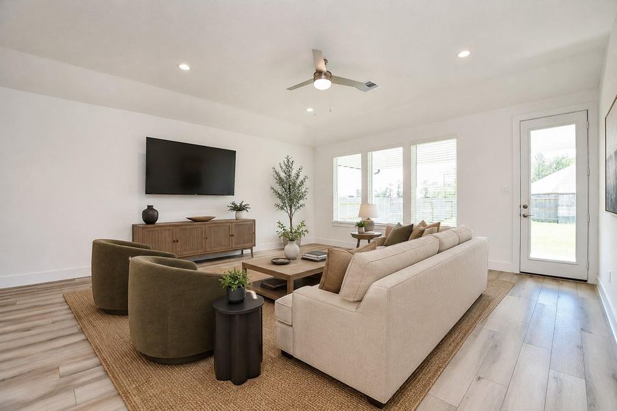 Another look at the main living space, where warm wood-look flooring flows toward the backyard and three large windows keep the room feeling bright and connected to the outdoors. *virtually staged*