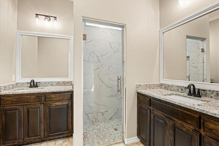 Bathroom with a marble finish shower, two vanities, and a textured wall