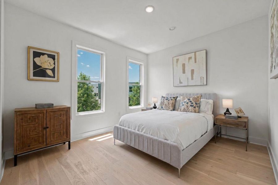 Bright secondary bedroom featuring expansive windows, recessed lighting, wide-plank wood flooring, and crisp modern finishes.