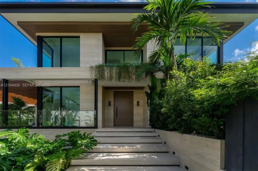 Modern two-story architectural exterior featuring stone tile cladding, wide-plank wood-finish soffits, expansive glass sliding doors, and a glass-paneled staircase railing