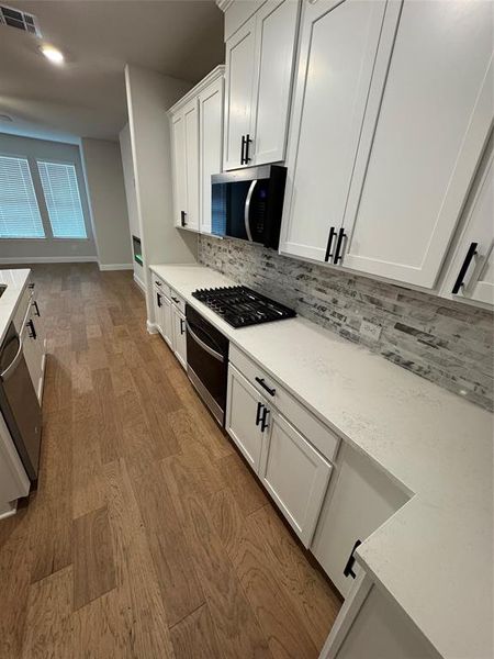 Kitchen featuring white shaker-style cabinetry with matte black hardware, quartz countertops, and a subway tile backsplash