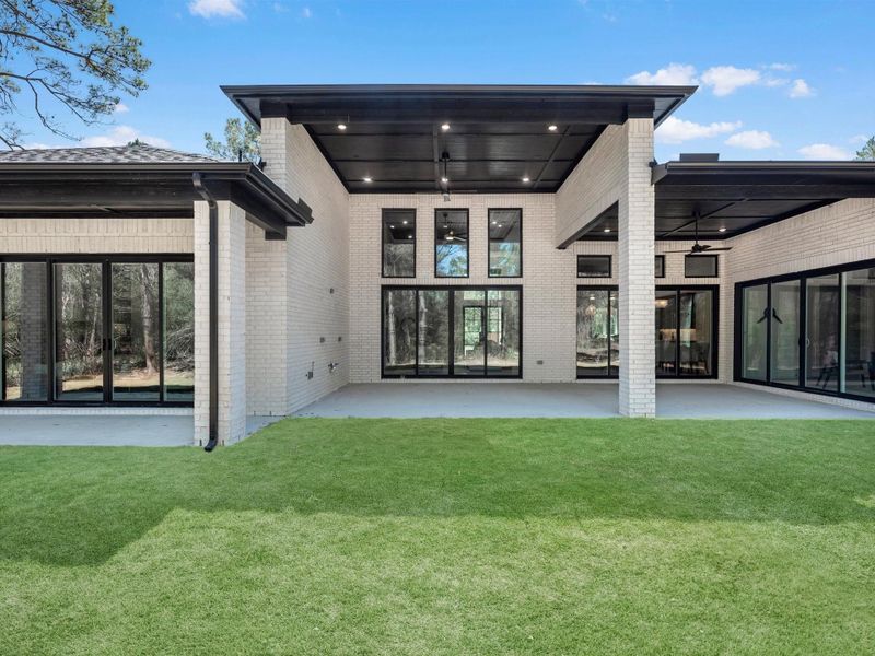 The rear elevation showcases seamless indoor-outdoor living, with a covered patio, expansive glass doors, and peaceful wooded views that create a private retreat.