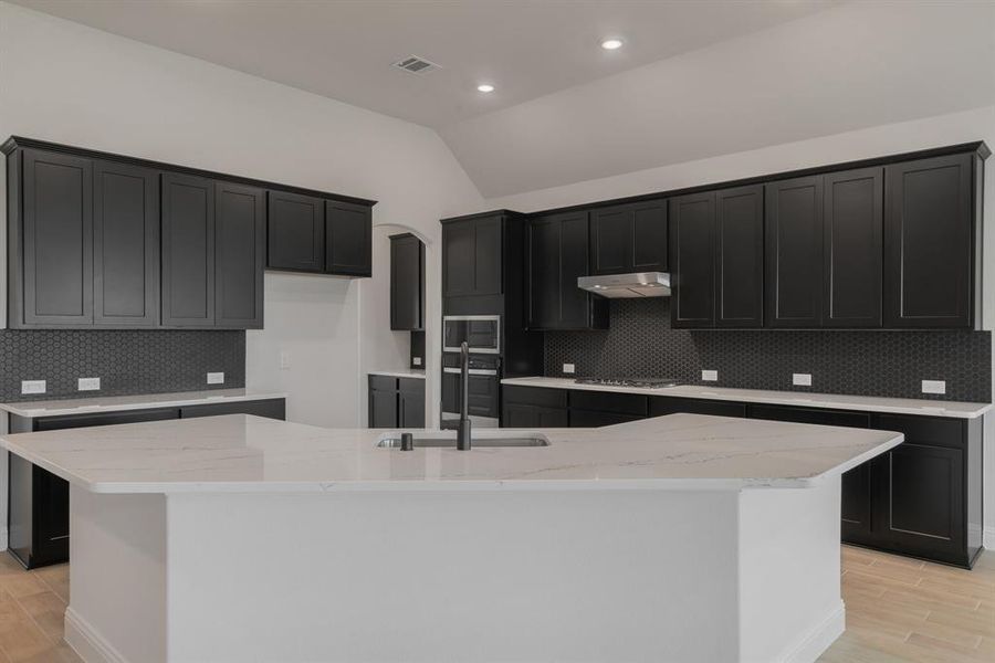 Kitchen with lofted ceiling, tasteful backsplash, and a kitchen island with sink